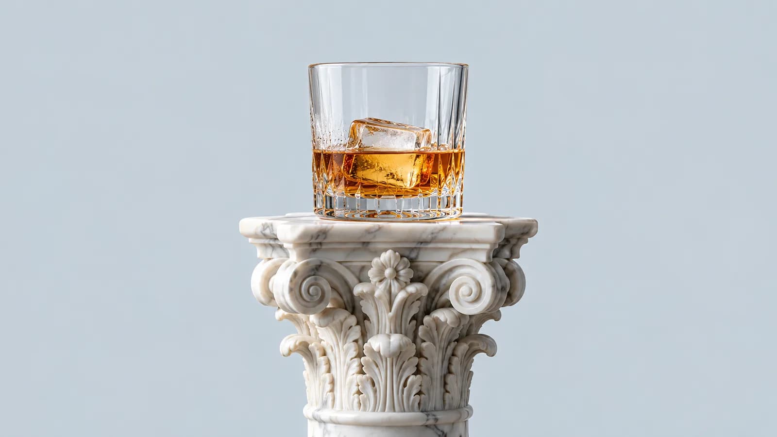 Bicchiere di whisky con ghiaccio appoggiato su un capitello corinzio in marmo, fondo grigio azzurro