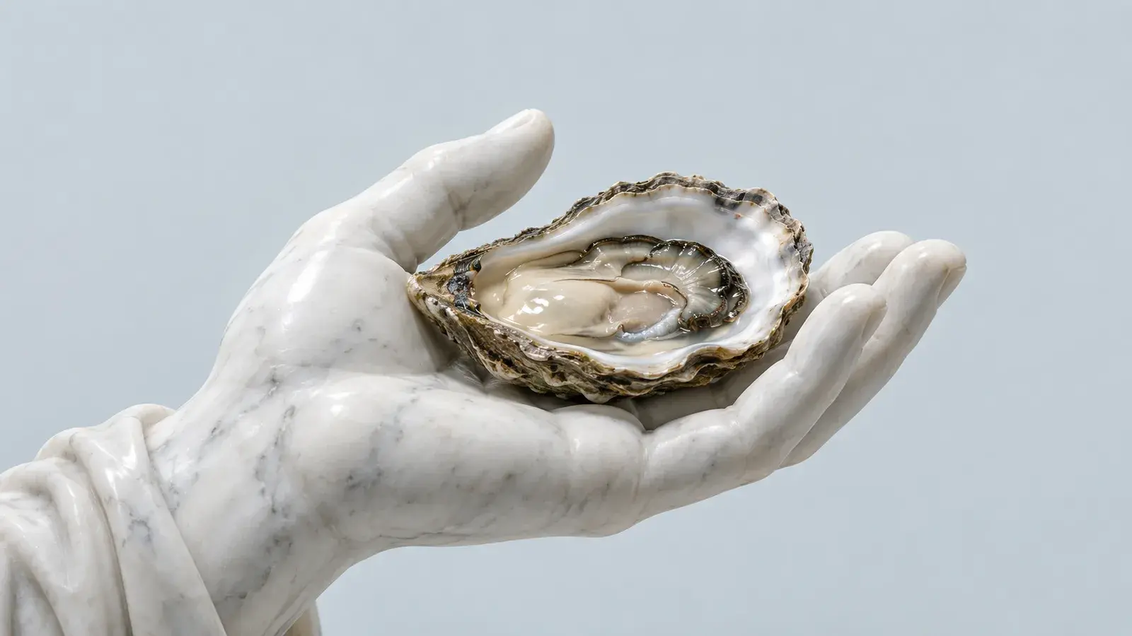 Mano di statua in marmo bianco che regge un'ostrica aperta su fondo grigio azzurro
